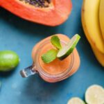 Papaya smoothie with half of a papaya, bananas, and lime in the background.