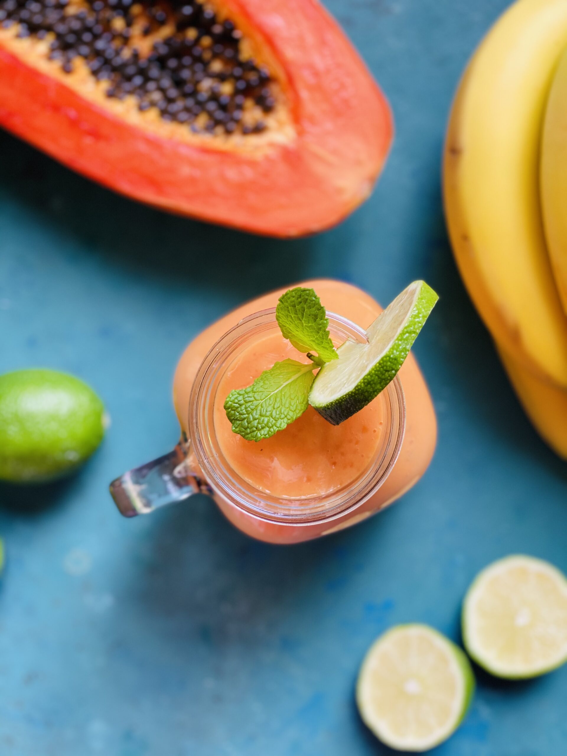 Papaya smoothie with half of a papaya, bananas, and lime in the background.