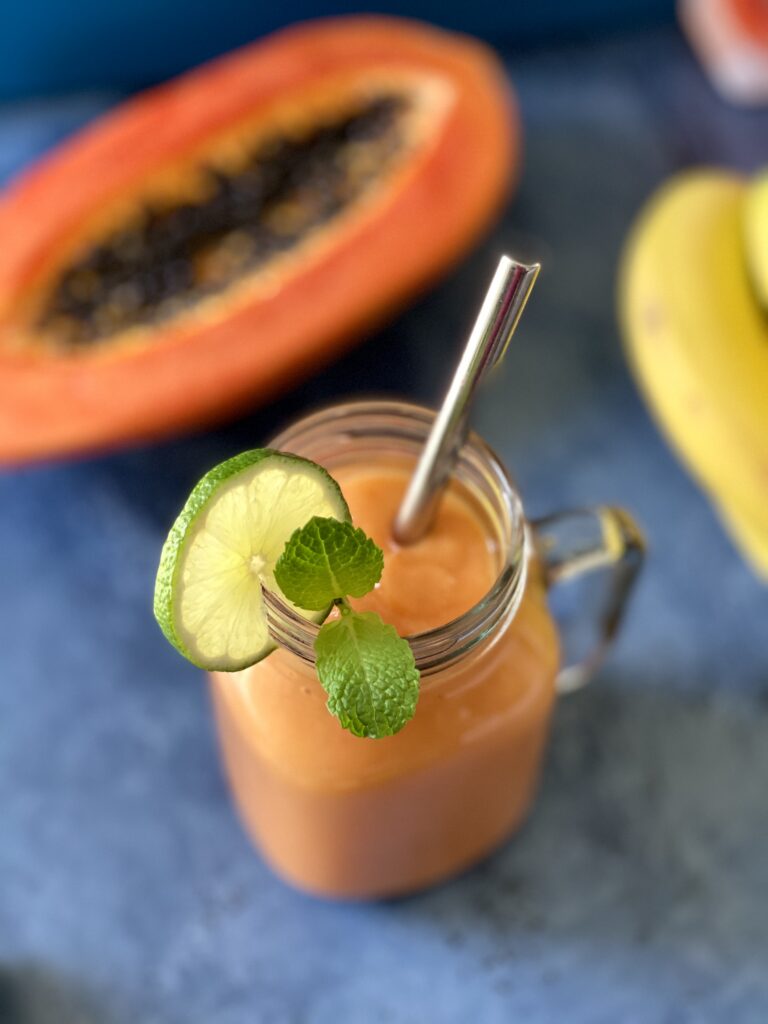 Papaya smoothie with half of a papaya, bananas, and lime in the background.