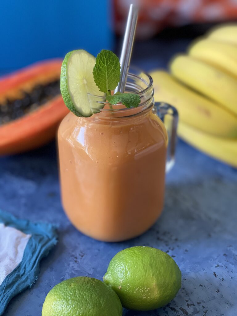 Papaya smoothie with half of a papaya, bananas, and lime in the background.