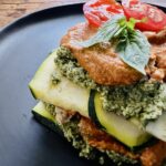 Raw vegan lasagna made with zucchini ribbons, pesto, and sun-dried tomato sauce on a black plate.