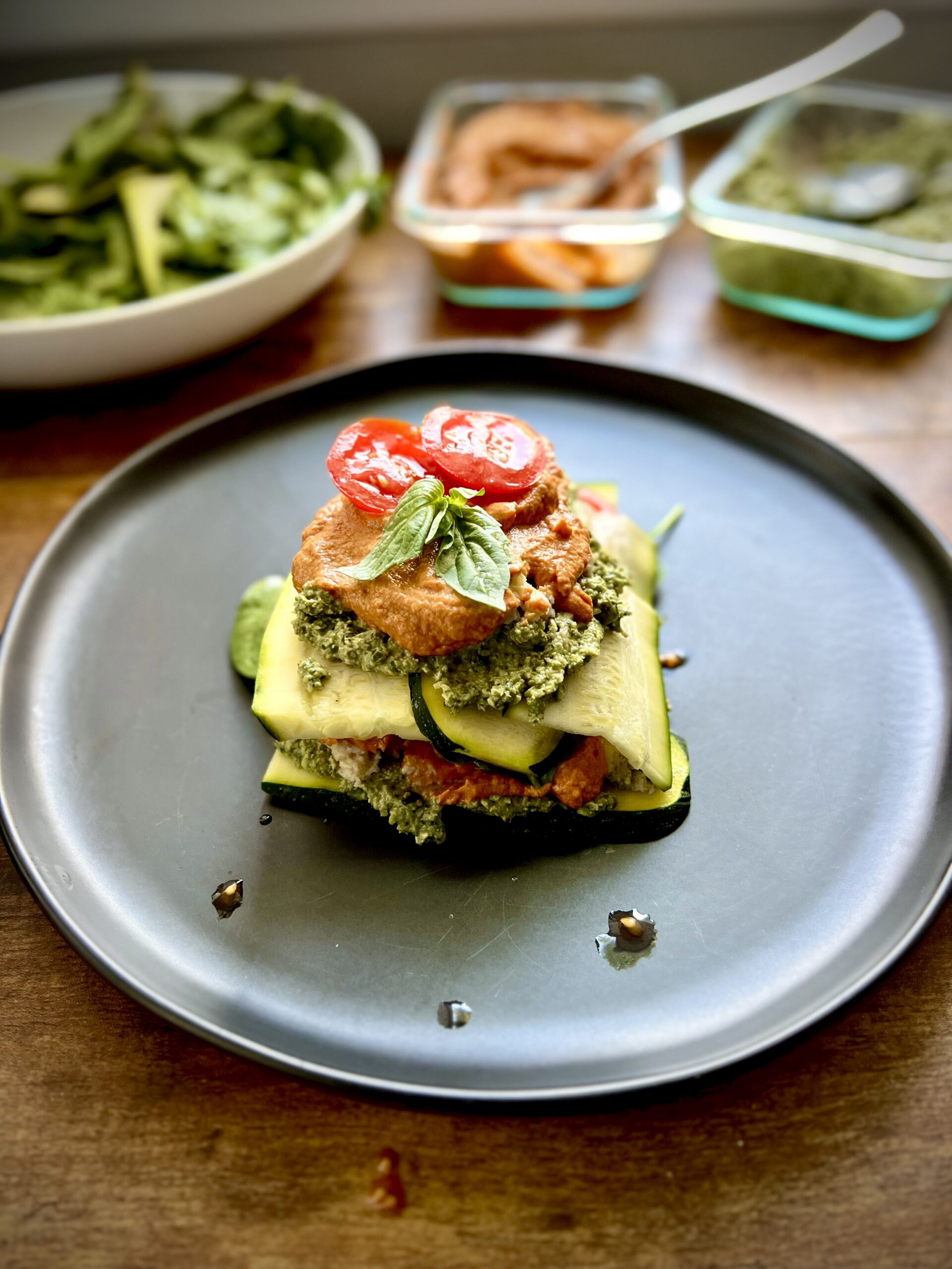 Raw vegan lasagna made with zucchini ribbons, pesto, and sun-dried tomato sauce on a black plate.