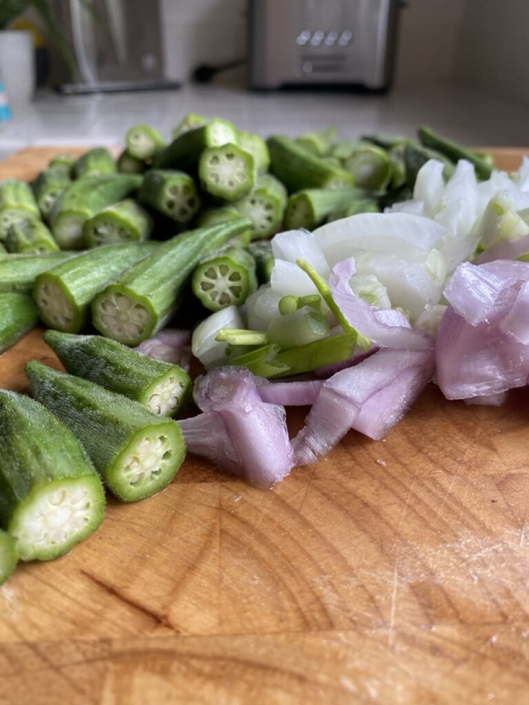 Fresh okra, diced onions, and minced garlic on a cutting board.