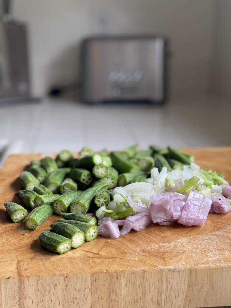 Fresh okra, diced onions, and minced garlic on a cutting board.