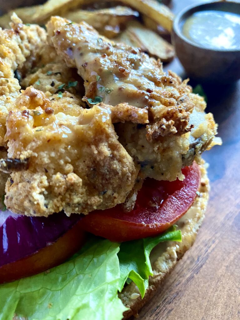 Close up of open-faced oyster mushroom sandwich with lettuce and tomatoes.
